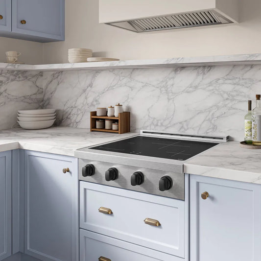 A ZLINE Autograph Edition 30 in. Paramount Induction Rangetop with 4 Element Cooktop in Satin Stainless Steel and Matte Black Accents (SINRTSZ-30-MB) installed in a kitchen with pale blue cabinets, a white marble backsplash, and a marble countertop.