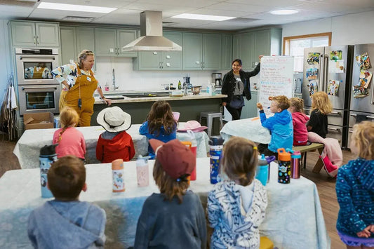 Instructors lead a group of children in a modern kitchen classroom featuring sage green cabinets and ZLINE appliances.