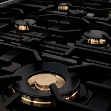 Close-up of a ZLINE gas cooktop featuring elegant gold brass burners and heavy-duty black cast iron grates.