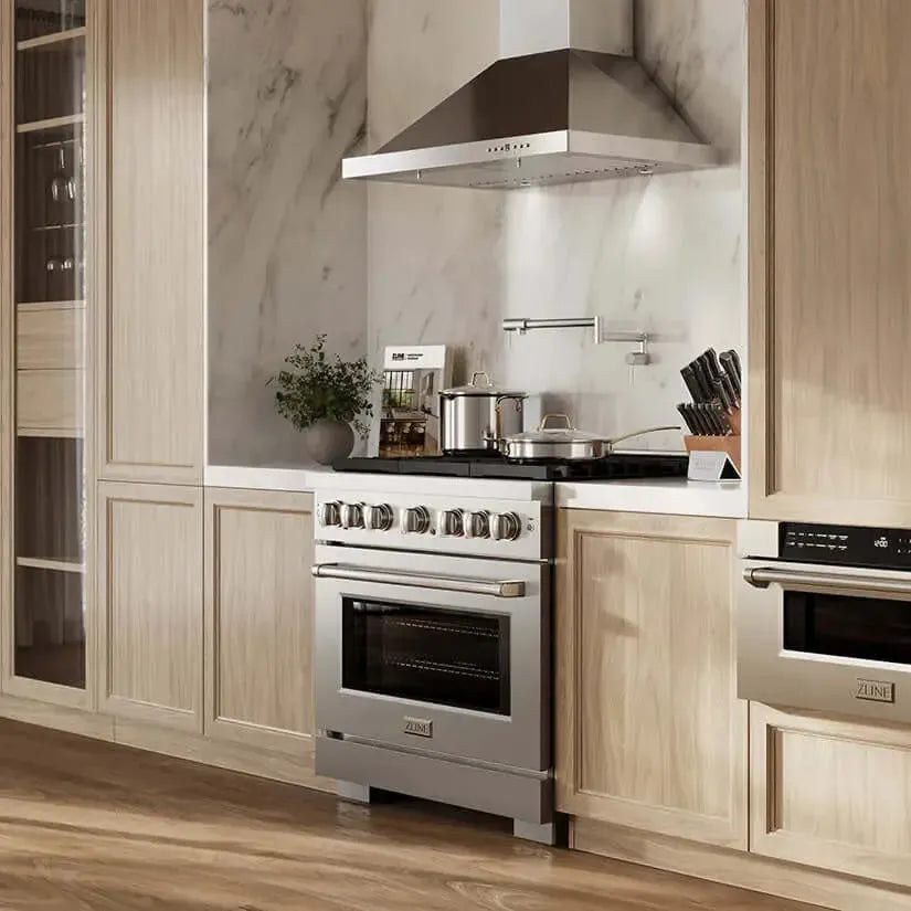 Stainless steel ZLINE gas range with professional hood in a modern kitchen with light wood cabinets and marble backsplash.