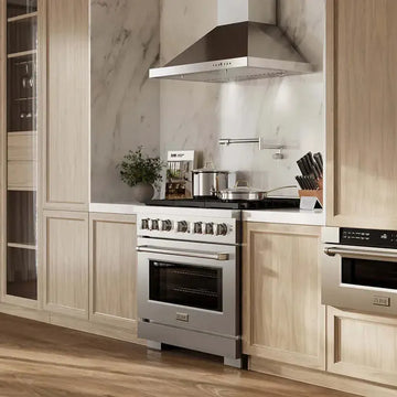 Stainless steel ZLINE gas range with professional hood in a modern kitchen with light wood cabinets and marble backsplash.