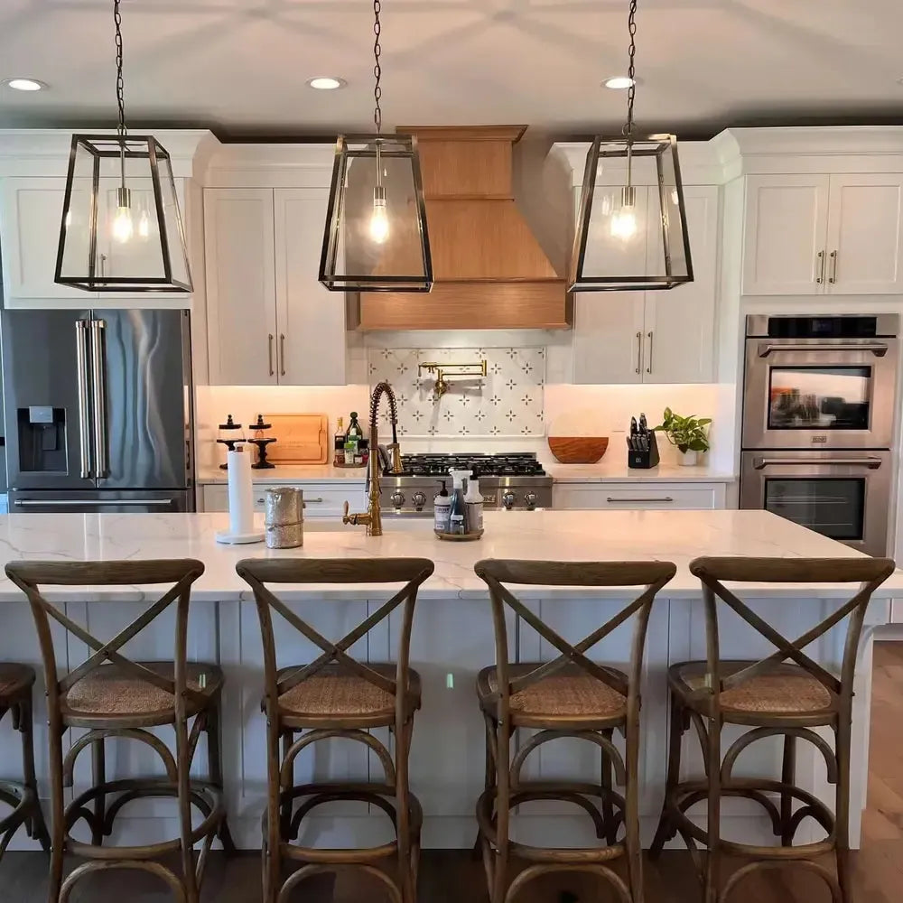 Modern white kitchen featuring a ZLINE range hood, stainless steel appliances, and a marble island with wooden stools.