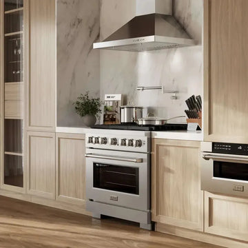 Stainless steel gas range with metallic knobs set in a modern kitchen with light wood cabinets and marble backsplash.