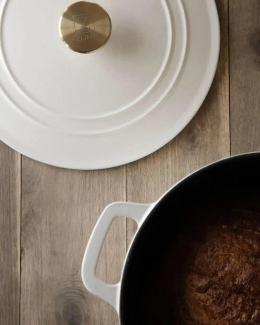 White enameled cast iron Dutch oven with a gold knob on a rustic wooden table.