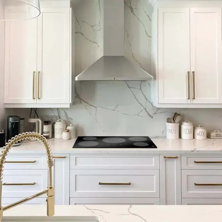 Black ZLINE induction cooktop set in a white marble kitchen with gold hardware and stainless steel range hood.