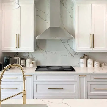 Black ZLINE induction cooktop set in a white marble kitchen with gold hardware and stainless steel range hood.