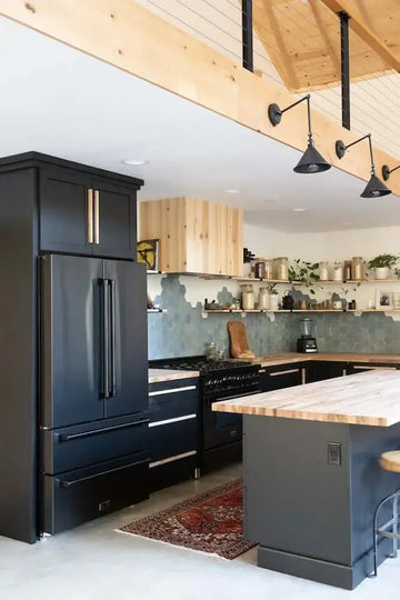 Modern kitchen with matte black cabinets, wood countertops, blue hexagonal tile backsplash, and vaulted wood ceiling.