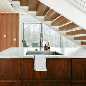 ZLINE Incline Kitchen Faucet in Chrome (INC-KF-CH) in a kitchen with wooden cabinets, white countertop, and staircase in the background.