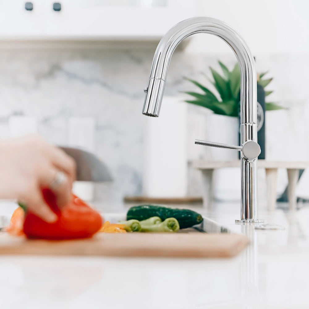 ZLINE Voltaire Pull Down Single Handle Kitchen Faucet in Chrome (VLT-KF-CH) with a blurred background of a kitchen setting.