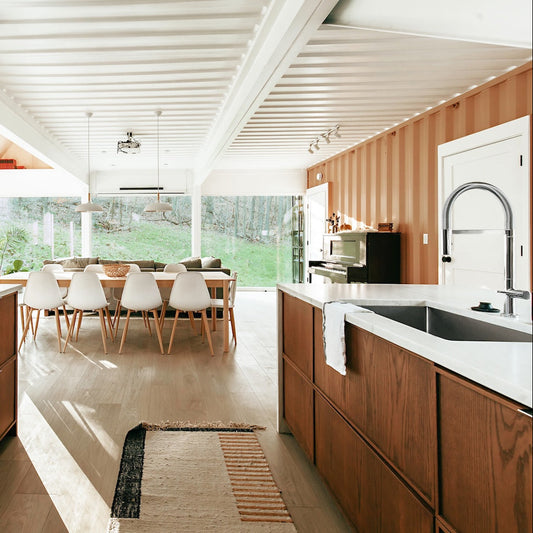 ZLINE Incline Kitchen Faucet in Chrome (INC-KF-CH) in a kitchen with wooden cabinets and white countertops, featuring a dining area in the background.