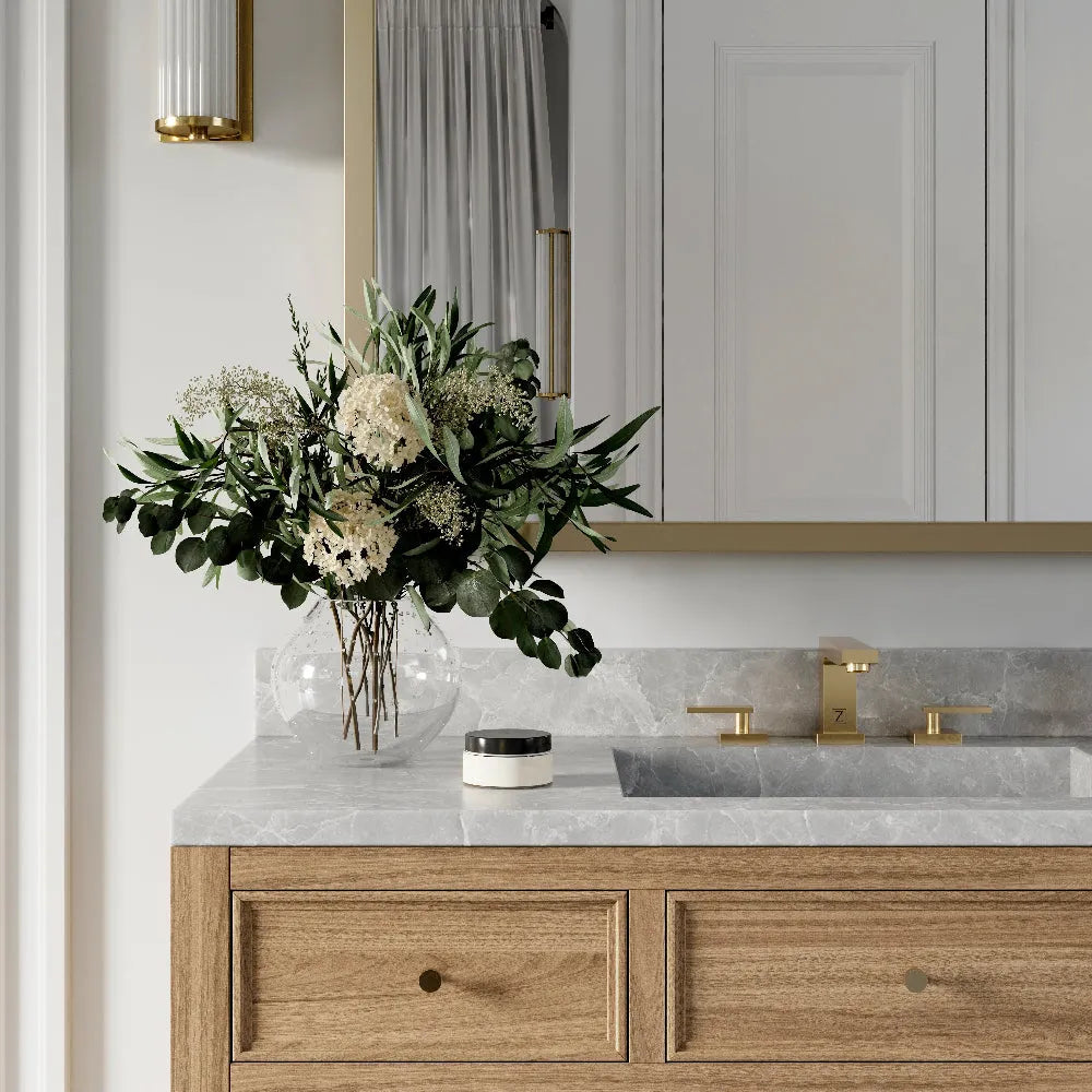 ZLINE Crystal Bay Widespread Bath Faucet in Champagne Bronze (CBY-BF-CB) on a bathroom vanity with wooden cabinets, marble countertop, and decorative flowers.