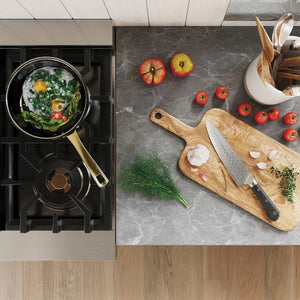 Cooktop with pot of food and kitchen counter with cutting board, knife, and vegetables.