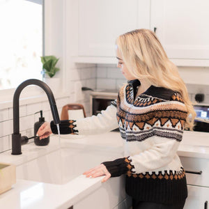 ZLINE Gemini Pull Down Kitchen Faucet in Matte Black (GEM-KF-MB) side, a woman turns the faucet on.