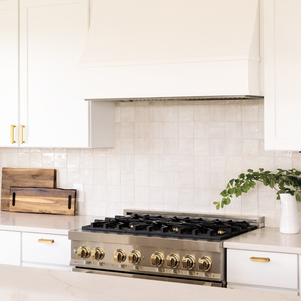 Farmhouse kitchen with a ZLINE Autograph Edition 36 in. 4.6 cu. ft. Legacy Dual Fuel Range with 6 Burner Gas Cooktop and Electric Convection Oven in Stainless Steel and Polished Gold Accents (RAZ-36-G) against a white tiled backsplash.