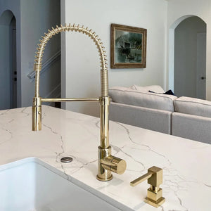 ZLINE Sierra Pull Down Spring Single Handle Kitchen Faucet in Polished Gold (SRA-KF-PG) on a marble countertop with a living room in the background