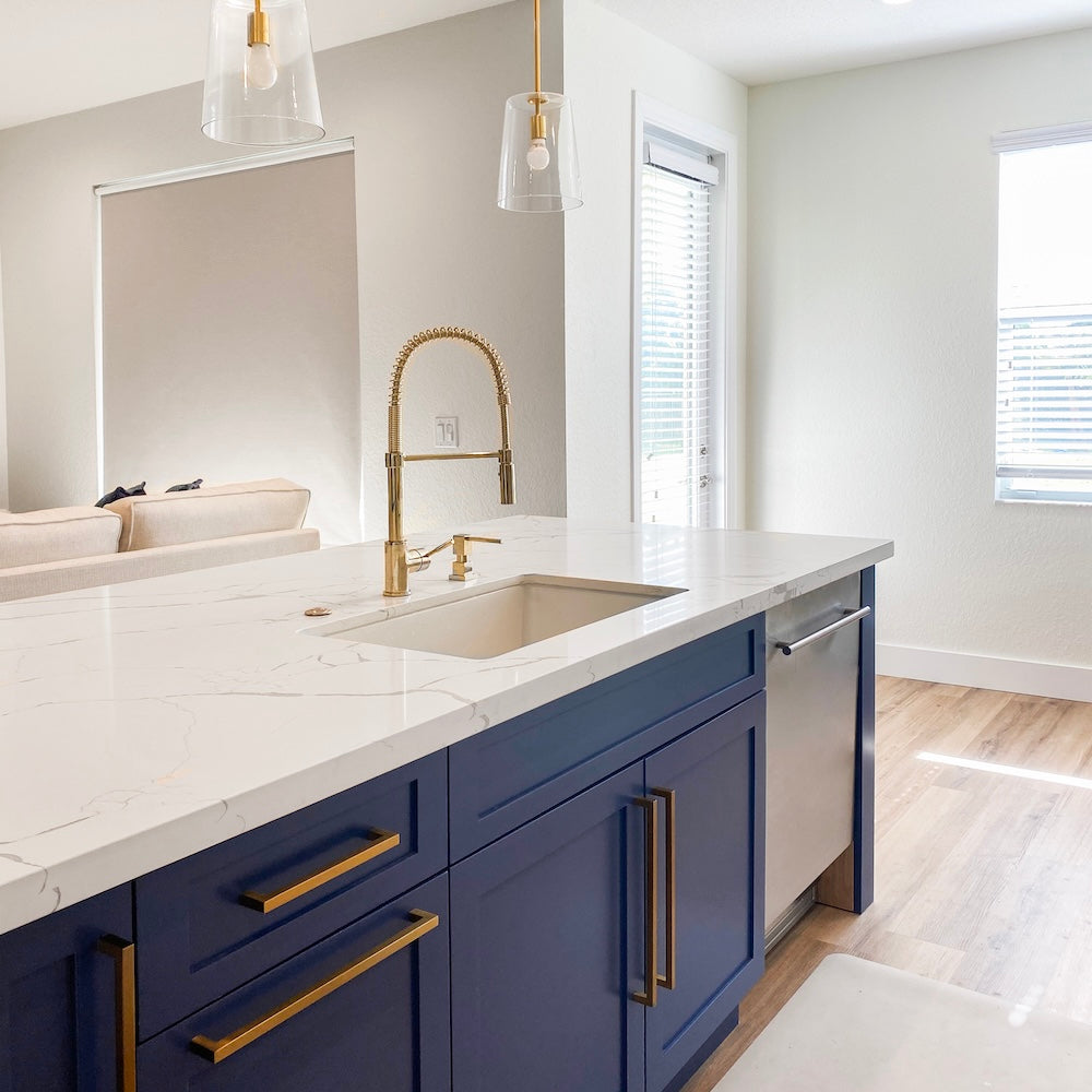 ZLINE Sierra Pull Down Spring Single Handle Kitchen Faucet in Polished Gold (SRA-KF-PG) in a kitchen with blue cabinets, gold accents, and white countertops.