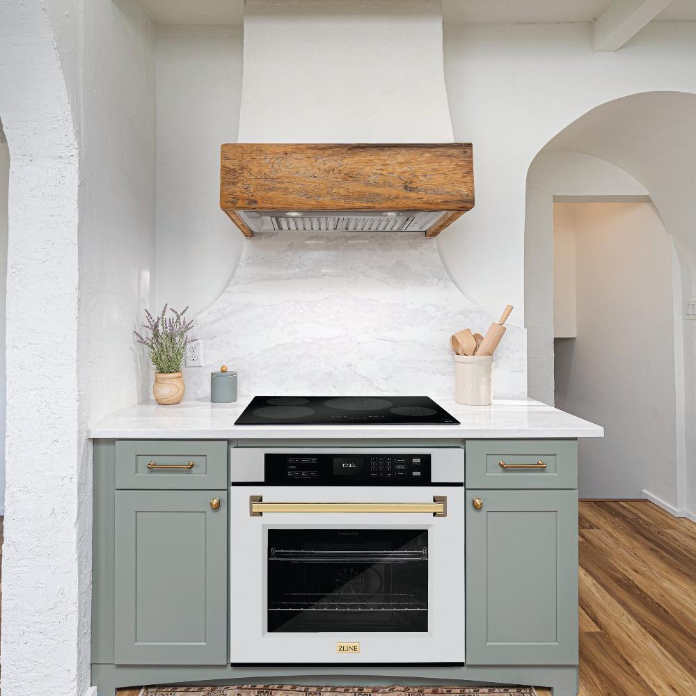 ZLINE Autograph Edition 30 in. Professional True Convection Single Wall Oven with Air Fry and Self Clean in Stainless Steel with White Matte Door and Polished Gold Handle (WASZ-WM-30-G) lifestyle in a rustic kitchen below induction cooktop with custom range hood.