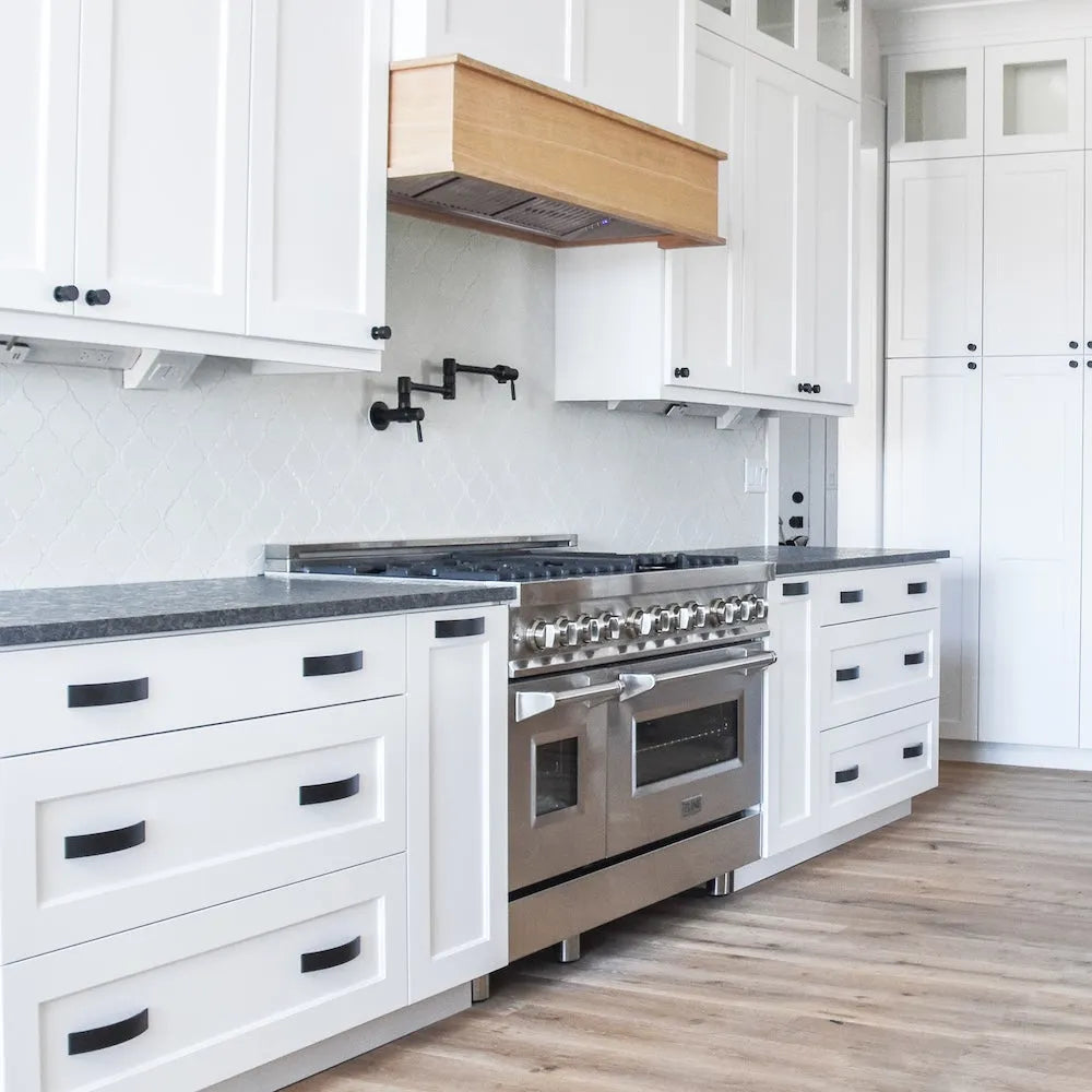 Farmhouse kitchen with white cabinets, stainless steel appliances, wooden flooring, and a custom range hood using a ZLINE 46 in. Ducted Wall Mount Range Hood Insert in Stainless Steel (695-46).