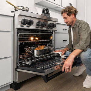 ZLINE Autograph Edition 30 in. 4.0 cu. ft. Legacy Dual Fuel Range with 4 Burner Gas Cooktop and Electric Convection Oven in Stainless Steel and Matte Black Accents (RAZ-30-MB) close-up, oven open, a man kneeling down checking the food inside.
