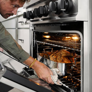 ZLINE Autograph Edition 30 in. 4.0 cu. ft. Legacy Dual Fuel Range with 4 Burner Gas Cooktop and Electric Convection Oven in Stainless Steel and Matte Black Accents (RAZ-30-MB) close-up, oven open, a man removing food from inside the oven, side.