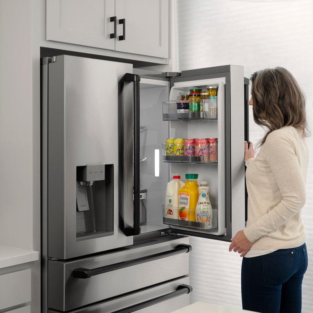 ZLINE Autograph Edition 36 in. 21.6 cu. ft Freestanding French Door Refrigerator with Water Dispenser in Stainless Steel with Matte Black Traditional Handles (RFMZ-W-36-MB) side, open, a woman looks inside refrigeration compartment.