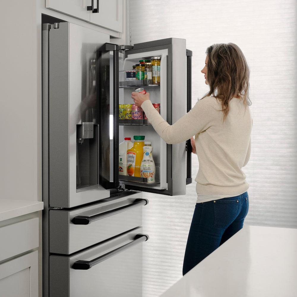 ZLINE Autograph Edition 36 in. 21.6 cu. ft Freestanding French Door Refrigerator with Water Dispenser in Stainless Steel with Matte Black Traditional Handles (RFMZ-W-36-MB) side, open, a woman reaches for a beverage inside refrigeration compartment.