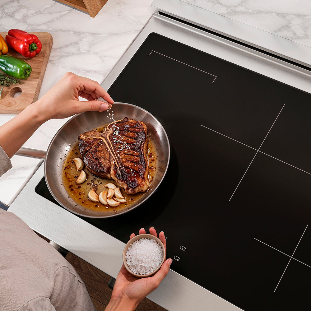 Person seasoning a steak in a pan on a ZLINE 30 in. Paramount Induction Rangetop with 4 Element Cooktop in Stainless Steel (SINRT30)