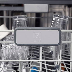 ZLINE Autograph Edition 24 in. Monument Series 3rd Rack Top Touch Control Tall Tub Dishwasher in Black Stainless Steel with Champagne Bronze Handle, 45dBa (DWMTZ-BS-24-CB) logo on dish rack with dishes in the background.