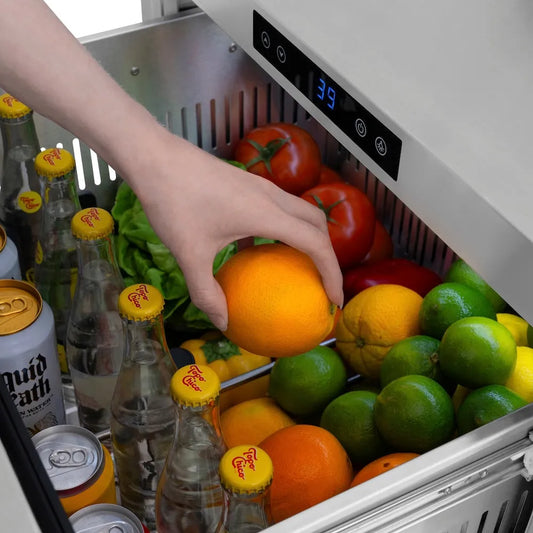 Hand reaching into a ZLINE Autograph Edition 24 in. Touchstone 168 Can Outdoor-Rated Dual Refrigerator Drawer with Black Stainless Steel Doors and Champagne Bronze Handles (RDSOZ-BS-24-CB) filled with fruits and drinks