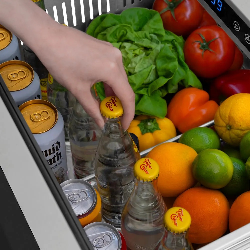 Hand reaching into a ZLINE Autograph Edition 24 in. Touchstone 168 Can Outdoor-Rated Dual Refrigerator Drawer with Black Stainless Steel Doors and Champagne Bronze Handles (RDSOZ-BS-24-CB) filled with drinks, fruits, and vegetables.