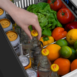 ZLINE Autograph Edition 24 in. Touchstone 168 Can Outdoor-Rated Dual Refrigerator Drawer with Black Stainless Steel Doors and Polished Gold Helix Handles (RDSOZ-BS-24-KG) hand reaching into refrigeration compartment filled with drinks, vegetables, and fruits.