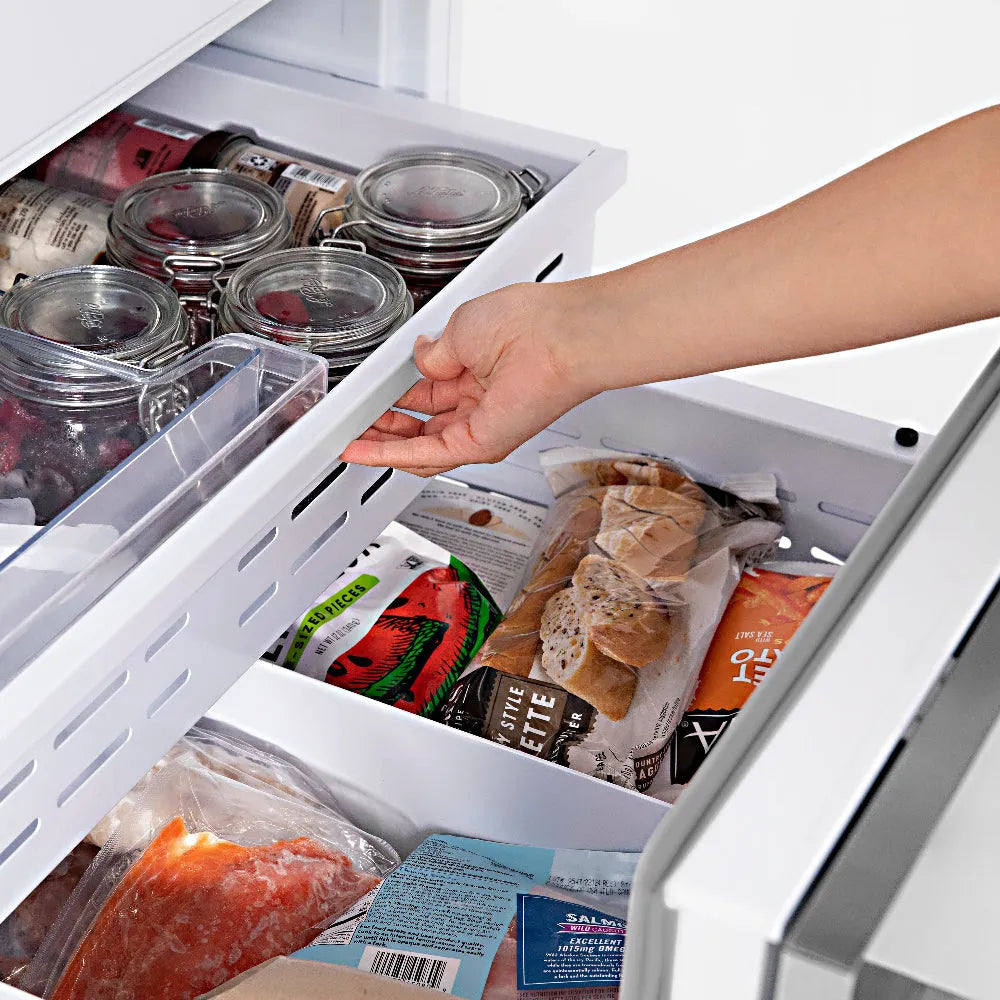 ZLINE Autograph Edition 30 in. 16.1 cu. ft. Panel Ready Built-In Bottom Freezer Refrigerator with Water Dispenser and Ice Maker with Matte Black Accents (RBIVZ-30-MB) hand reaching into bottom freezer drawer filled with various food items.