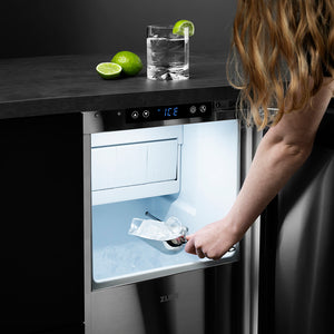 ZLINE Autograph Edition 15 in. Touchstone Gourmet Ice Maker with Drain Pump and Black Stainless Steel Door with Champagne Bronze Helix Handle (IGMDZ-BS-15-KCB) person scooping ice out of ice maker with a drink and limes on the counter above.