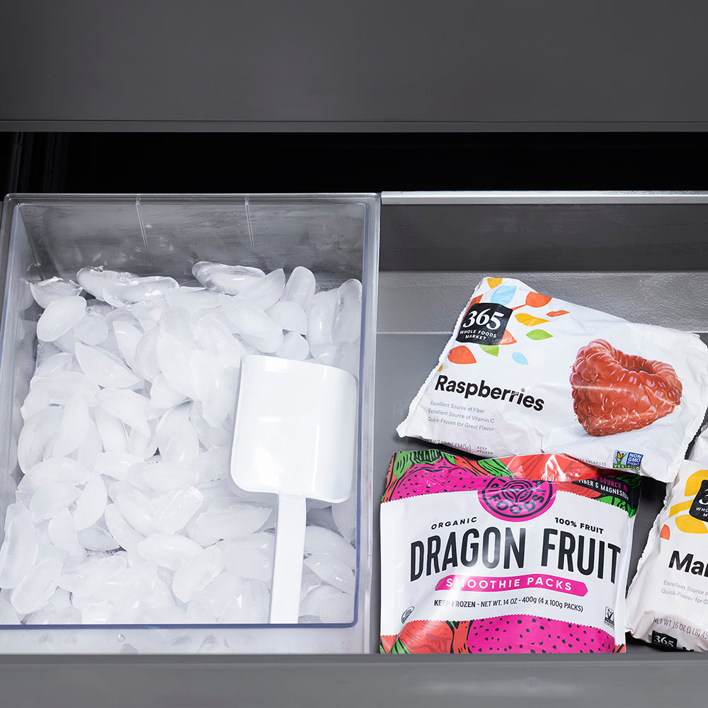 ZLINE Autograph Edition 36 in. 19.6 cu. ft. French Door Built-In Bottom Freezer Refrigerator with Water Dispenser and Ice Maker in Black Stainless Steel with Stainless Steel Interior and Polished Gold Helix Handles (SRBIVZ-BS36KG) bottom freezer drawer open with fruit packages including dragon fruit and raspberries next to a container of ice cubes.