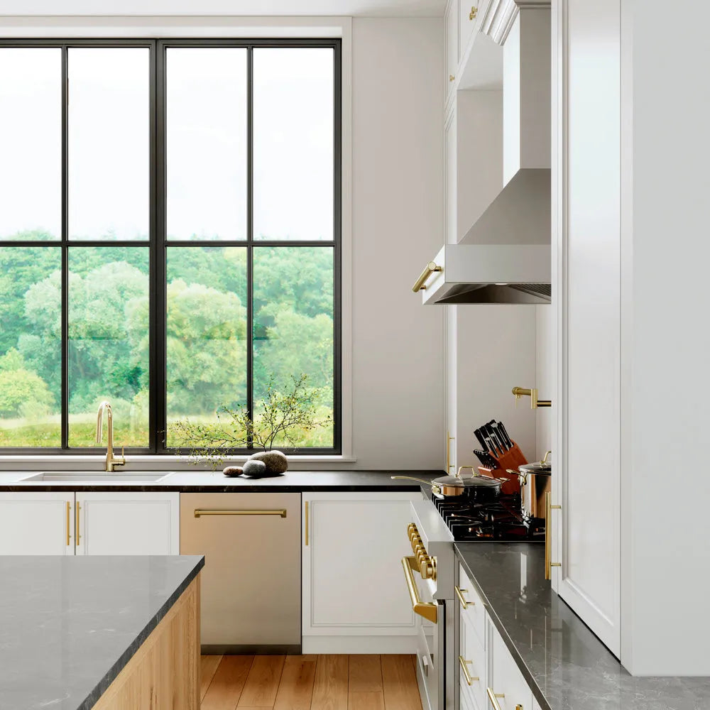 ZLINE Autograph Edition 24 in. Tallac Series 3rd Rack Dishwasher with Auto Door Open Drying, 51dBa, Stainless Steel Panel with Polished Gold Handle (DWVZ-304-24-G) in a kitchen with white cabinets, black countertops, and a large window view of greenery.