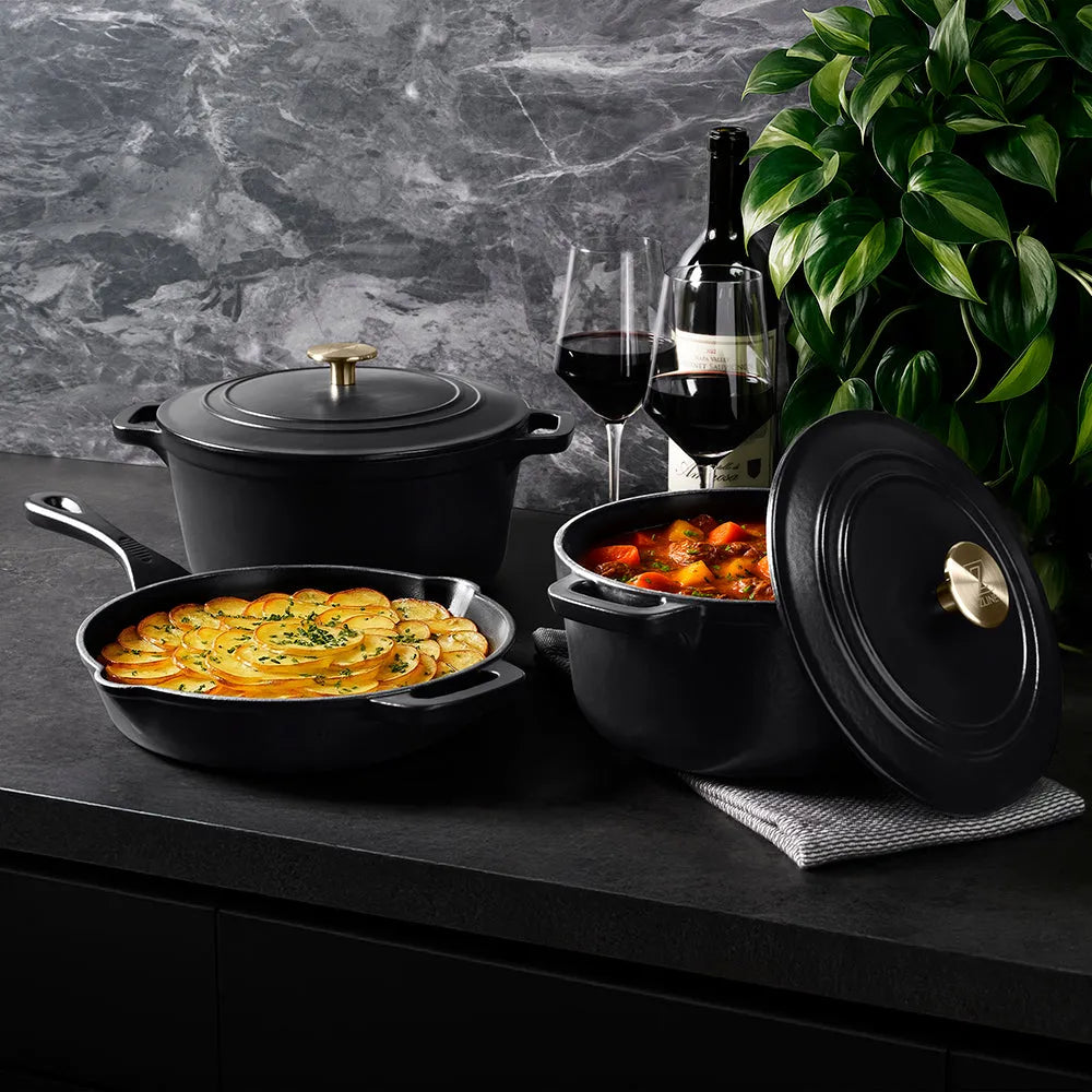 ZLINE 5-Piece Enameled Cast Iron Cookware Set in Black Matte (CWSETS-BLM-5) on a dark surface with food and wine glasses.