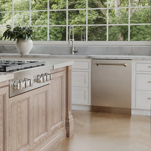 ZLINE 24 in. Monument Series 3rd Rack Dishwasher with Auto Door Open Drying, 44dBa, Stainless Steel Panel (DWMT-304-24) in a kitchen with wooden cabinets, stainless steel cooktop, and a large window view of greenery.