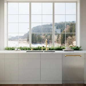 ZLINE Autograph Edition 24 in. Monument Series 3rd Rack Dishwasher with Auto Door Open Drying, 44dBa, Stainless Steel Panel with Polished Gold Handle (DWMTZ-304-24-G) in a kitchen with large window view of a lake and trees