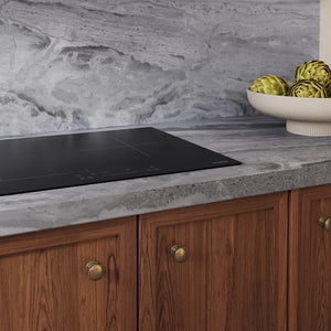 ZLINE 24 in. Induction Cooktop with Anti-Scratch Glass and 3 Elements (FCIND-24) embedded in a gray marble countertop, set against a matching gray marble backsplash and wooden cabinets with brass knobs. A white bowl of artichokes sits on the counter.