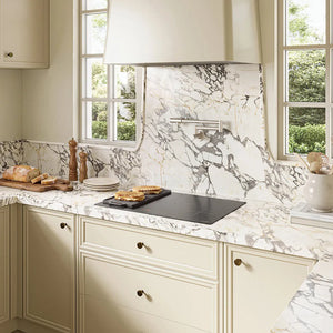 Cream-colored kitchen cabinets with a matching marble-look backsplash and countertop, featuring a ZLINE 30 in. Induction Cooktop with Anti-Scratch Glass and 4 Elements (FCIND-30), stainless steel range hood, and windows with white frames.