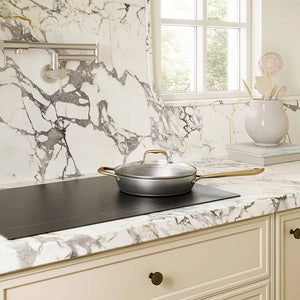 A ZLINE 30 in. Induction Cooktop with Anti-Scratch Glass and 4 Elements (FCIND-30) with a silver pan and lid on a white and gray marble countertop in a bright kitchen setting.
