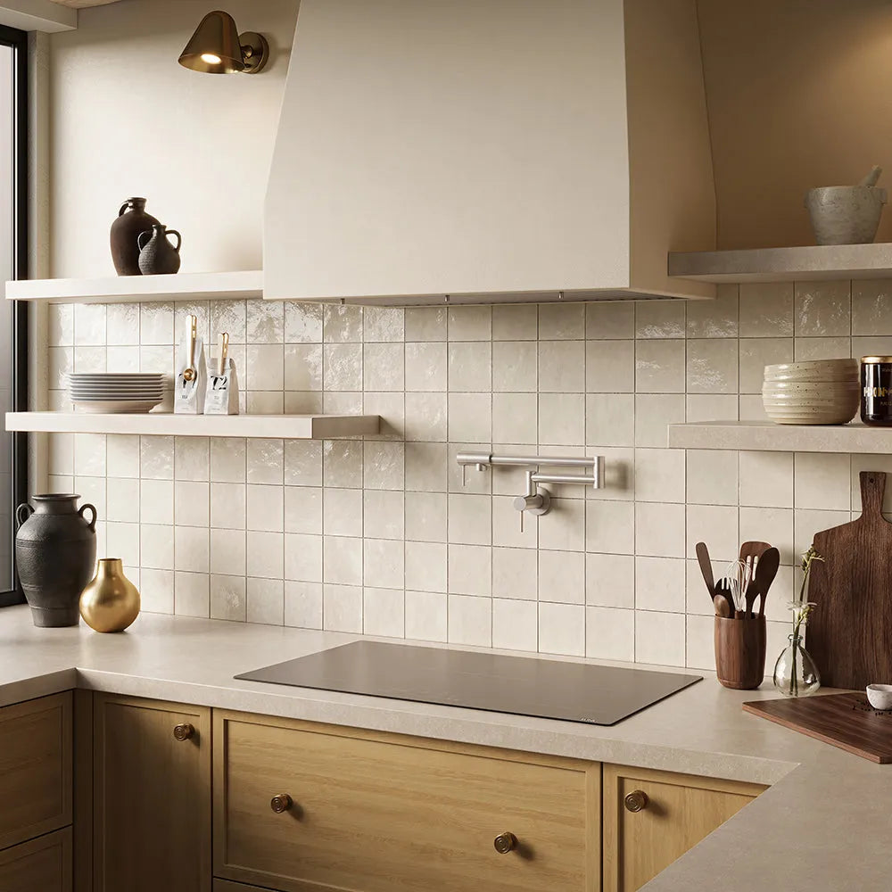 A kitchen interior with cream subway tile backsplash, light wood cabinetry, open floating shelves with ceramic vessels, a ZLINE 36 in. Induction Cooktop with Anti-Scratch Glass and 5 Elements (FCIND-36), and a large cream range hood.