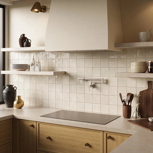 A kitchen interior with cream subway tile backsplash, light wood cabinetry, open floating shelves with ceramic vessels, a ZLINE 36 in. Induction Cooktop with Anti-Scratch Glass and 5 Elements (FCIND-36), and a large cream range hood.