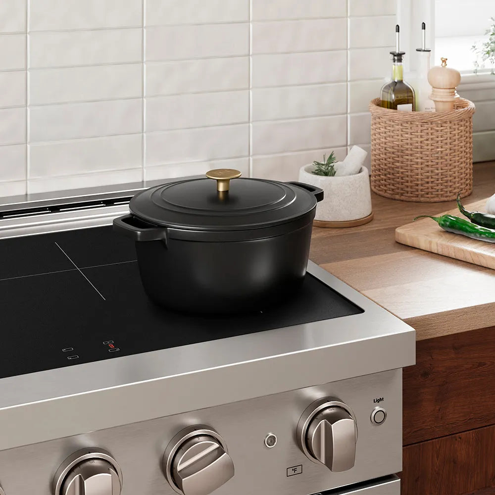 Black enameled cast iron cookware on an induction kitchen range with a tiled wall and wooden countertop in the background.