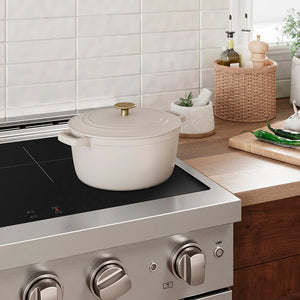 White enameled cast iron cookware on an induction kitchen range with a tiled wall and wooden countertop in the background.