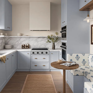 A compact modern kitchen with light blue cabinets, white marble backsplash, ZLINE Autograph Edition 30 in. Paramount Induction Rangetop with 4 Element Cooktop in Satin Stainless Steel and Matte Black Accents (SINRTSZ-30-MB), a small round wooden table, and a blue-and-white patterned upholstered bench.