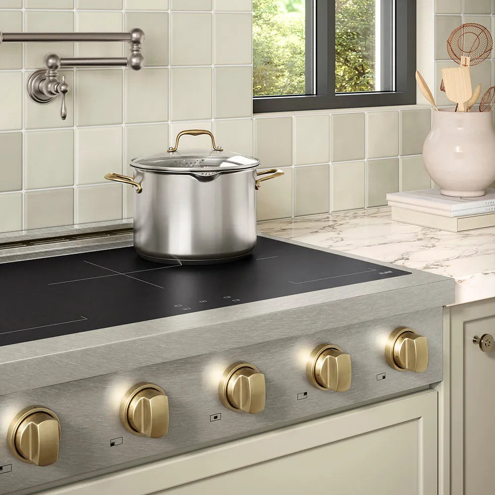 ZLINE Autograph Edition 36 in. Paramount Induction Rangetop with 5 Element Cooktop in Satin Stainless Steel and Champagne Bronze Accents (SINRTSZ-36-CB) in a designer kitchen with marble backsplash, light blue cabinets, angled.