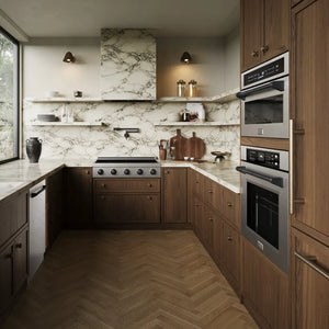 A modern kitchen interior with dark wood cabinetry, marble countertops and backsplash, a herringbone wood floor, ZLINE Autograph Edition 36 in. Paramount Induction Rangetop with 5 Element Cooktop in Satin Stainless Steel and Matte Black Accents (SINRTSZ-36-MB), and open shelving with decorative items.