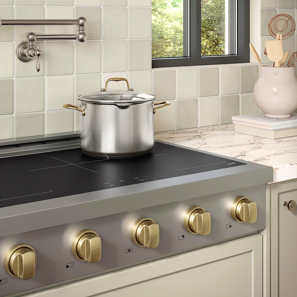 ZLINE Autograph Edition 36 in. Paramount Induction Rangetop with 5 Element Cooktop in Stainless Steel and Champagne Bronze Accents (SINRTZ-36-CB) in a designer kitchen with tiled backsplash, light green cabinets, angled.