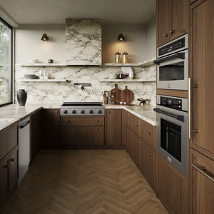 A modern kitchen interior with dark wood cabinetry, marble countertops and backsplash, a herringbone wood floor, ZLINE Autograph Edition 36 in. Paramount Induction Rangetop with 5 Element Cooktop in Stainless Steel and Matte Black Accents (SINRTZ-36-MB), and open shelving with decorative items.